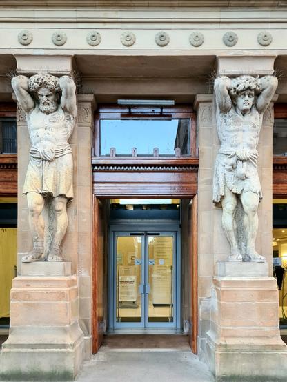 Two large, sculpted Atlas figures at the entrance to a Glasgow library.