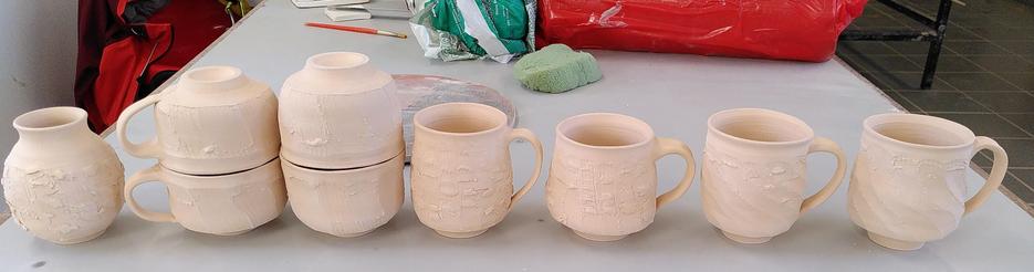Line of ceramic faceted wheel thrown mugs, cups and a vase which are bisque fired.
Ligne de mugs, tasses et vase en céramique tournés et facettés sortant de la cuisson biscuit.