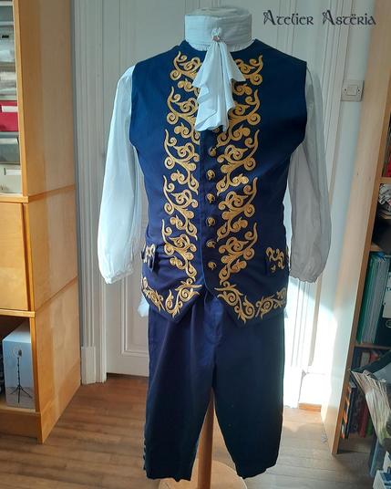 Costume pour GN (jeu de rôle grandeur nature). D'inspiration XVIIe siècle, il est bleu foncé avec plein de décorations dorées. Il est composé d'une chemise, d'une culotte à pont, d'un col à jabot, d'une gilet, d'un manteau et d'une ceinture
