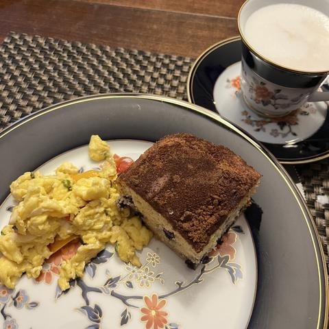 A plate with scrambled eggs, a square piece of coffee cake topped with a cinnamon crumble, and a matching china cup of frothy tea. The plate has floral designs with a blue border