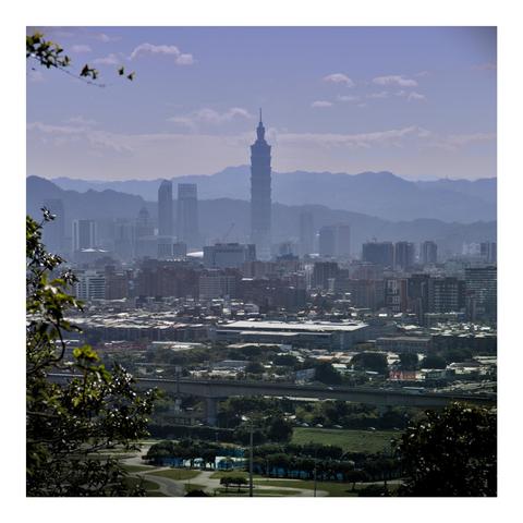 This image showcases a cityscape of Taipei, Taiwan, with the iconic Taipei 101 skyscraper prominently standing in the center. The city extends around it, featuring numerous high-rise buildings, mid-rise apartments, and lower residential areas. In the foreground, there is lush greenery, trees, and what appears to be a park or golf course. A raised highway or railway line cuts across the lower part of the image. The background consists of mountain ranges that provide a natural contrast to the urban environment. The atmosphere has a slightly hazy feel, with soft lighting suggesting it might be early morning or late afternoon. The image is framed with tree branches on the left side, adding depth and a natural touch to the urban scene.