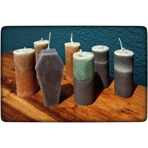 Es stehen ein paar Kerzen, aus Klorollen in dunklen Farben, stehen auf einem Holztisch vor einer blauen Wand. Eine Sargkerze in schwarz steht links vorne.