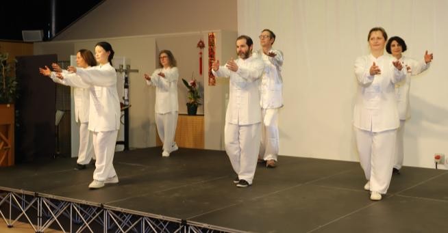 Sur une scène, sept personnes portant la même tenue blanche présentent une démonstration de taiji quan.
(photo : www.gouvenelstudio.com)