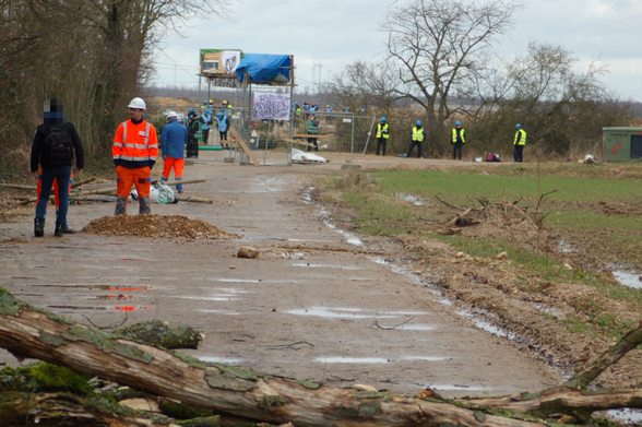 Barrikaden auf der RWE-Werkstraße am Rand des Manheimer Erbwalds, dazwischen steht der Werkschutz mit Bauhelmen.