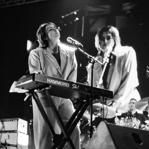 Black and white shot. Angel stands at her keyboard staring up at the sky. Her oversized suit was originally bright yellow in real life, but it looks like a cool grey in this black and white shot. The light on her left shoulder (right for us) is reflected brightly off her hair.  In the background the screen shows her shot from above and directly at her eyes, but is slightly out of focus due to the shallow depth of field and the shot being focused on the real Angel.  

I sadly had a lens stolen an hour after this happened. This festival stressed me out with social anxiety working for pitchfork in their staff team shooting bts content, while not actually being on the official photo team. So I felt like I was on the island of misfit toys.