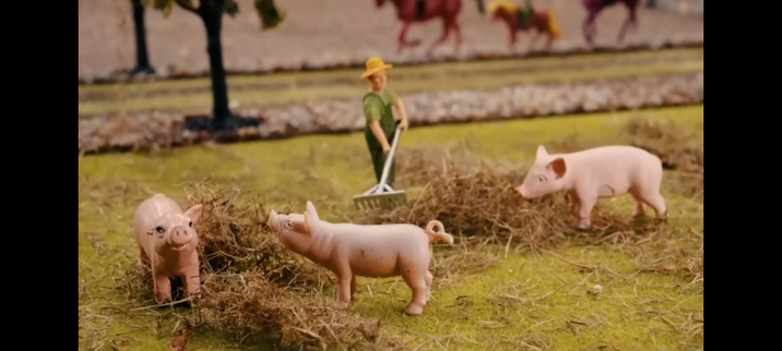Billede af plastikbonde sammen med tre plastikgrise, og nogle plastiktræer og plastikheste i baggrunden.