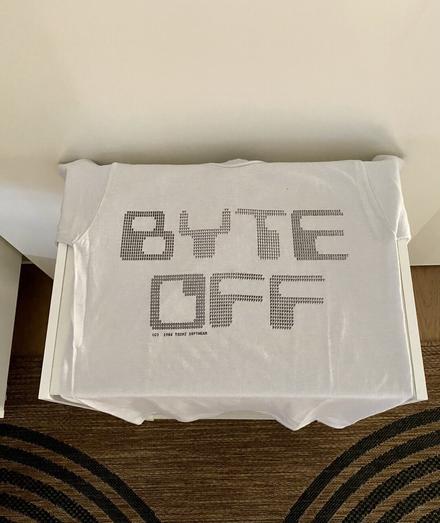White tee shirt with the words BYTE OFF printed on it. Each letter is formed from very small letters representing the larger letter. Such as the “B” is made of numerous capital Bs, the “Y” from numerous Ys, etc.