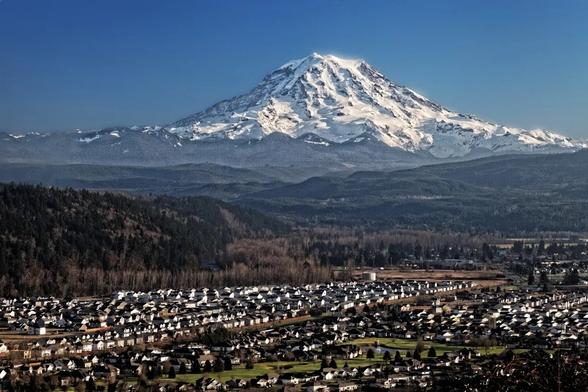 photo - Mount Rainier, a snowcapped volcano, looms over Puyallup Valley near Orting, Washington. The prospect of a lahar — a swiftly moving debris flow caused by melting snow and ice typically during a volcanic eruption — poses a threat to surrounding communities.