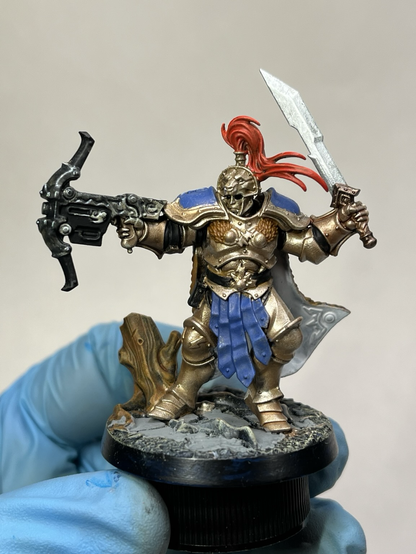 Front view of work in progress Stormcast Eternal Vanguard: a fully armored warrior with crossbow, sword, and cape. Golden armor with blue trim and fur cape. Crossbow has dark silver fittings.
