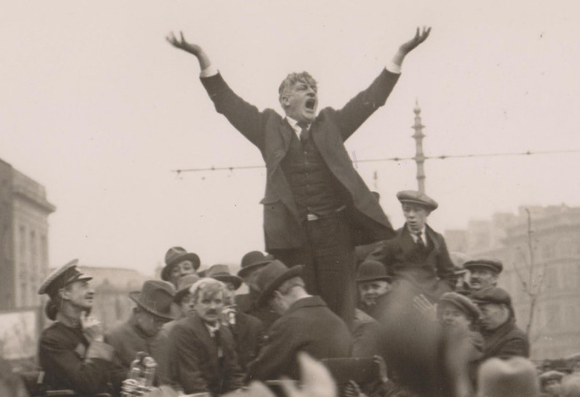 Larkin giving a speech on O'Connell Street shortly after his return from America where he can be seen standing above the crowds with his arms held aloft in full flow.