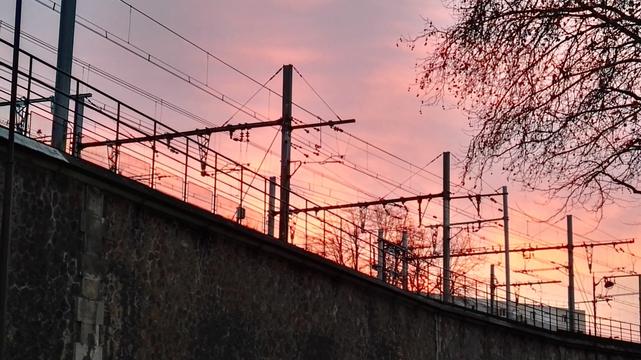 overhead lines on the RER B line. sky is red and orange behind.