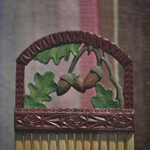 Closeup of a heddle carved from a solid piece of birch. It has a motif of oak leafs and acorns.