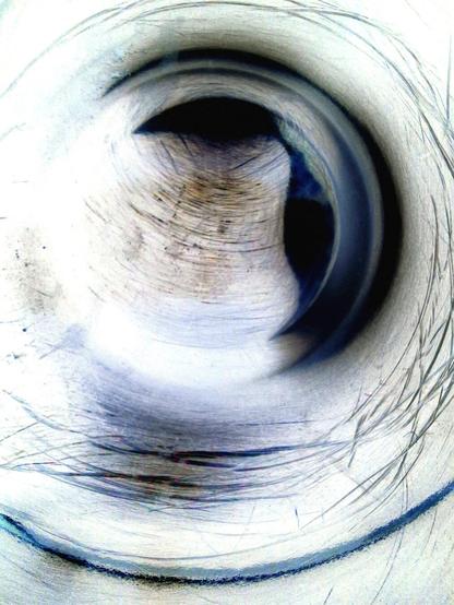 A prominent, dark circular spot in the center. The area surrounding this spot is textured with various shades of blue, white, and gray, and has visible circular lines similar to scratches. The dark circular spot certainly gives off those enigmatic, black-hole vibes.