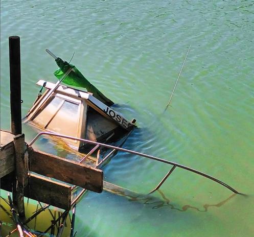 Una barca o pequeño barco pesquero, con el nombre Josep, aparece semihundido en unas aguas verdosas