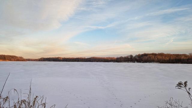 A frozen lake at the beginning of the golden hour. The sky above is blue and the clouds are tinged pink and yellow by the setting sun.
