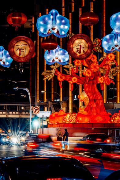Moving and stationary vehicles provide a base from which festive light sculptures emerge. A perfect lighting storm for the pair in the middle to take a shot.
