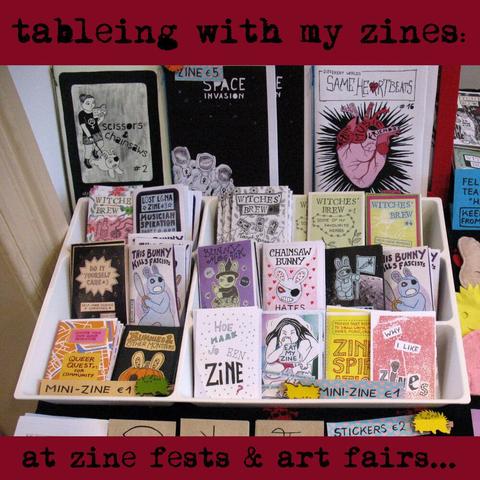Table with mini-zines in cutlery box and bigger zines behind. Titles include "Same Heartbeats" and "Chainsaw Bunny Hates Everyone". Text: "Tableing with my zines at zine fests art fairs."