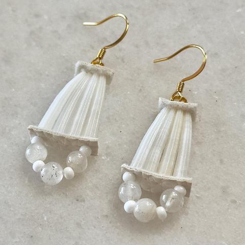 A pair of small dentalium earrings against a marble background. Each earring has four shells, held together at each end with strip of white faux leather, with some beads on the bottom and gold hooks at the top.