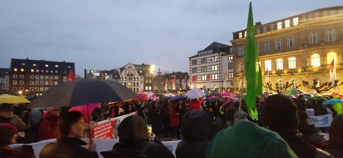 Demonstrierende, z.T. mit Regenschirmen, auf dem Burgplatz in Düsseldorf.