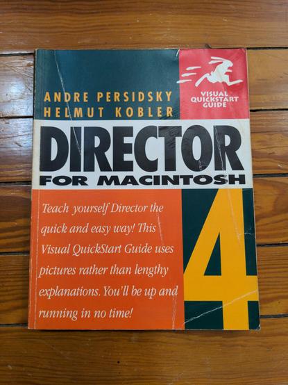 A paperback book with a slightly creased cover lying on a wooden floor. At the upper let is ANDRE PERSIDSKY HELMUT KOBLER in yellow on red. A white rabbit, running like a human is printed in a red square in the upper right with white text reading VISUAL QUICKSTART GUIDE. DIRECTOR FOR MACINTOSH in black on white in the center. Below that to the left in white serif text on orange is Teach yourself Director the quick and easy way! This Visual QuickStart Guide uses pictures rather than lengthy explanations. You'll be up and running in no time! To the right of that in the same gold on green as the authors' names is a giant 4.