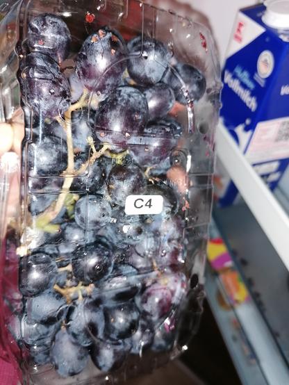 Eine Packung dunkle Weintrauben mit einem kleinen Aufkleber auf der Packung: "C4"