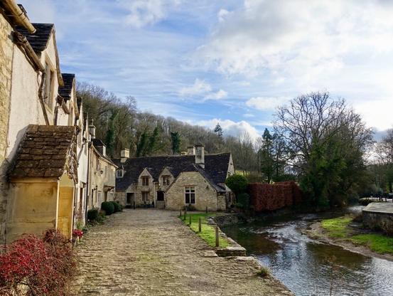 A mews of cottages, built of Cotswold stone, next to a stream in England.