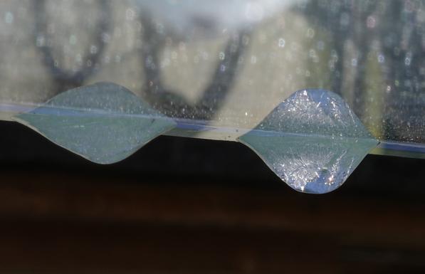Two ice drops hang under a glass plate and are reflected from it. The drop in focus has captured some blue sky and rays of sunshine and looks like an opal.