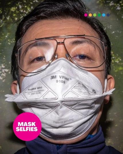 A close-up selfie of a person wearing a white 3M VFlex N95 respirator and large glasses with slightly fogged-up lenses. The background shows a green leafy environment. A pink circle in the bottom left corner contains the text "MASK SELFIES." At the top, a row of six colorful dots is aligned.