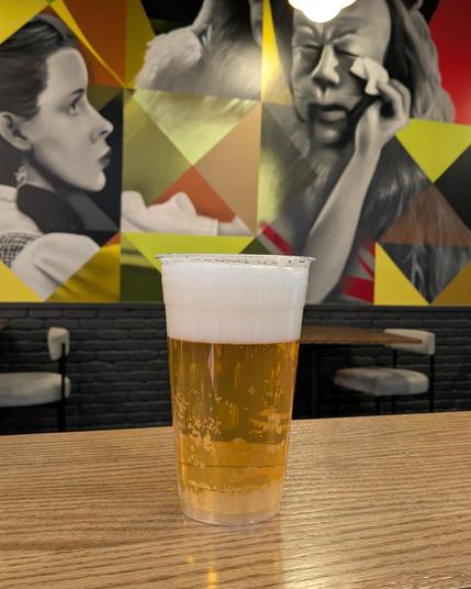 Hard cider in a plastic cup. Mural of Dorothy and the Cowardly Lion in the background.