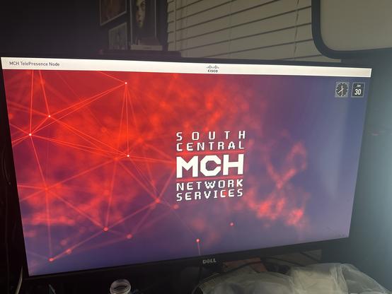 A picture of a computer display on my cluttered desk displaying the OSD of a Tandberg C60.

The wallpaper is bright and dark reds, with abstract geometric lines, and has the text "SOUTH CENTRAL MCH NETWORK SERVICES" in the middle.

Along the top is an information bar that reads "MCH TelePresence Node", with a Cisco logo, and the current time and date.