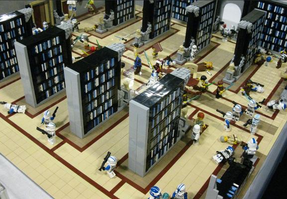 Photo of a lego model of a Jedi library. Several star wars characters can be seen and it looks as if  a battle has broken out. The book cases are very tall and are in black grey and blue giving the model an ominous look.