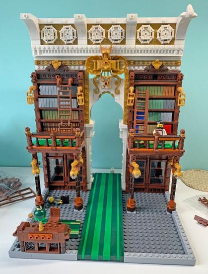 Photo of a lego model depicting a classically styled private library complete with mezzanine level to reach the tall book shelves. There is also a ladder, books behind glass and a fancy carpet. The decoration is highly ornamental with with fancy light fittings, lamps, and ornate balustrades on the mezzanine.