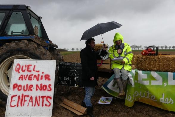 Caroline Duvelle du collectif en interview, à côté d’elle un tracteur avec une pancarte : Quel avenir poiur nos enfants/