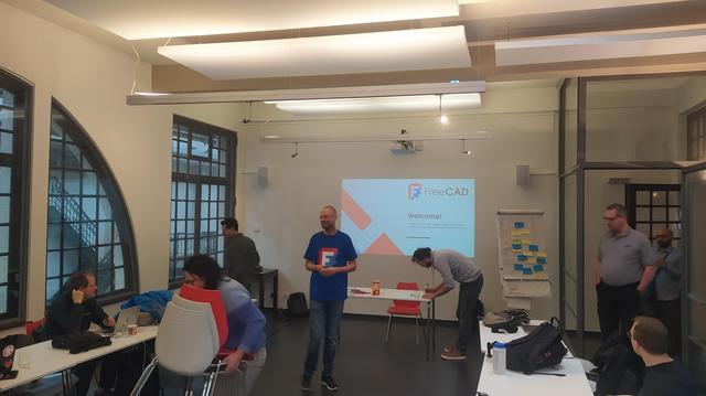 Yorik and FreeCAD developers in a work room with a welcome screen in the background.