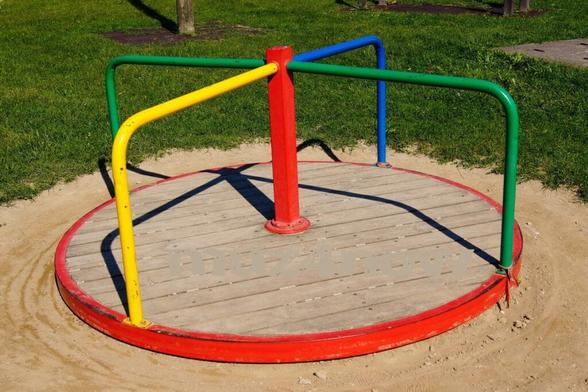 An old, merry-go-round representing the federated social networks. The base is made of wood and shows wear. The handles and center pole are made of metal with the center painted red and the four handrails painted with 2 painted green, 1 blue, and 1 yellow.