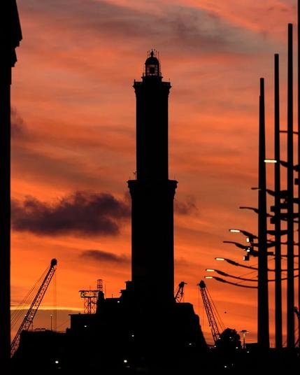 Silhouette of the Lanterna lighthouse in Genoa old harbour against a red sky at sunset