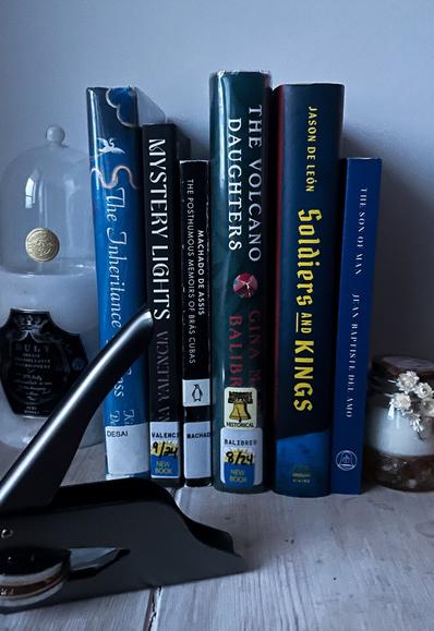 A picture of six books on a nightstand. Also in the photograph are two candles and an embosser