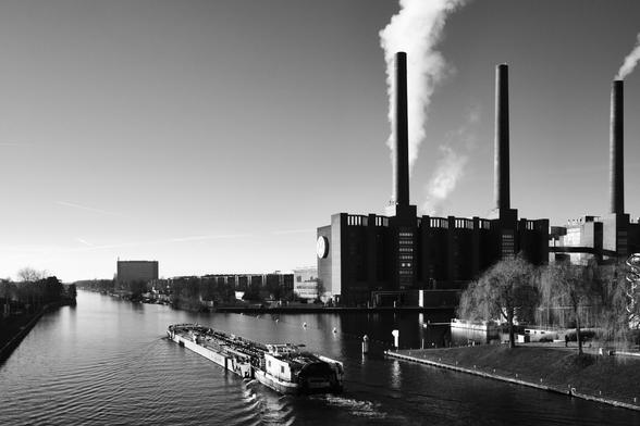 Schwarzweiß Foto der Volkswagenfabrik in Wolfsburg, der Mittlandkanal im Vordergrung mit einem Binnenfrachter, black and white photograpy of the fabric of Violkswagen cars in Wolfsburg, a canal infornt with a boat sailing away