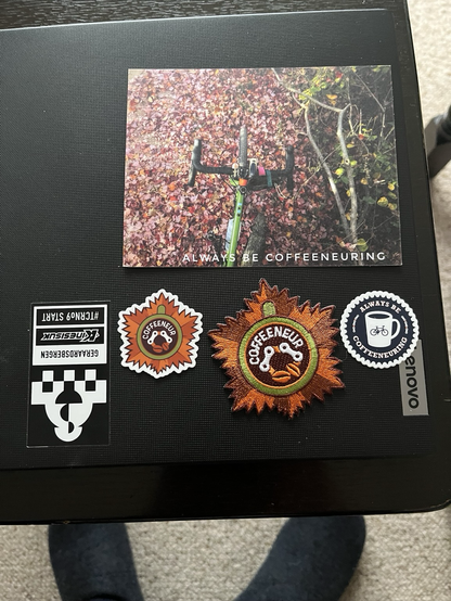 Two ‘Coffeeneuring’ stickers, a patch and card on top of a laptop.