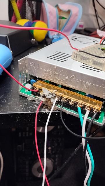 Photo of a 12v power supply sitting on the edge of a desk with wires coming off it. In the center is the remains from the catastrophic failure of two