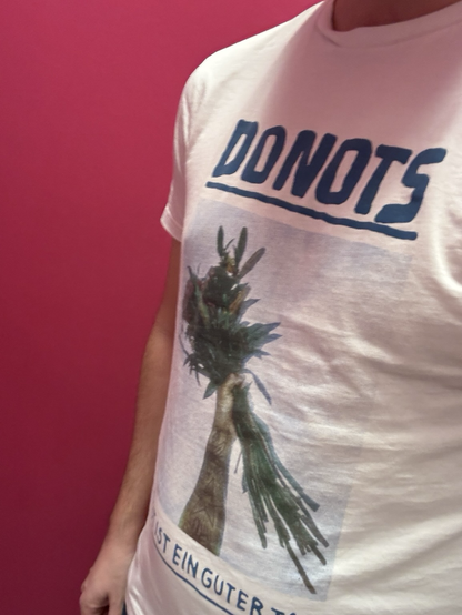Ein Selfie, das meinen Oberkörper zeigt, der in ein feines Donots T-Shirt gehüllt ist. Auf dem Shirt ist eine Hand abgebildet, die einen Blumenstrauß in die Luft hält. Darüber steht der Name der Band, darunter „Heut ist ein guter Tag“.