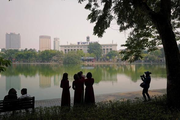 A group of women standing close to the lake, another taking photos of them. All are visible mainly as silhouettes in front of the lake scenery.