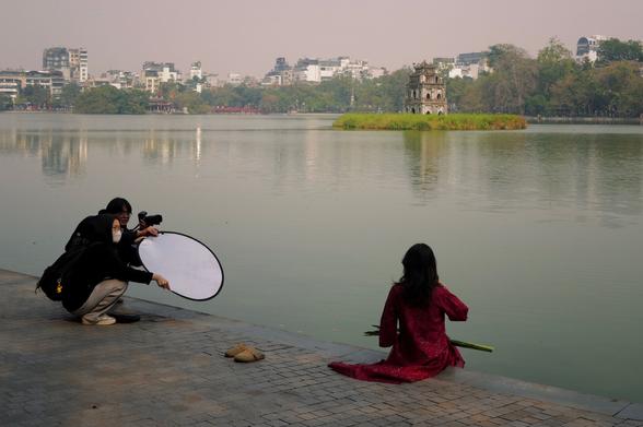 Woman sitting close to the lake, in the background a photographer and a person holding a reflector