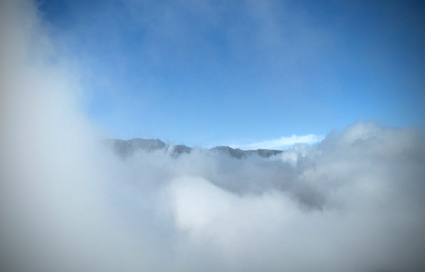 Von Kraterrand auf 1880m geht der Blick über den riesigen Krater der Caldera, der mit Wolken gefüllt ist. Auf der anderen Seite ragen die Felsspitzen knapp aus den Wolken empor.