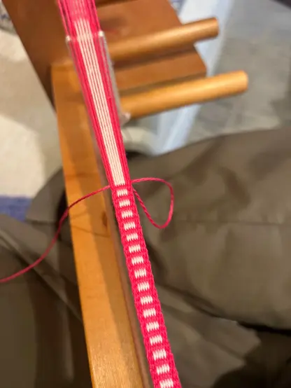 A narrow hot pink and pale pink band bring woven on an inkle loom
