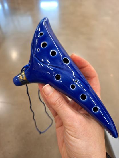 A blue ceramic 12-hole ocarina with a triforce symbol in gold on the mouthpiece. You can tell this is a real instrument and not a toy because of its size and by the distribution of the finger holes, they are in two lines of 4 (for the 4 fingers of each hand).  There is also space to hold onto the instrument at each end even when all the finger holes are uncovered.