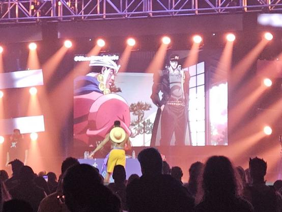 A man in a bit less of a Monkey D. Luffy cosplay looks upon a screen containing a frame of JoJo's Bizarre Adventure Stardust Crusaders.