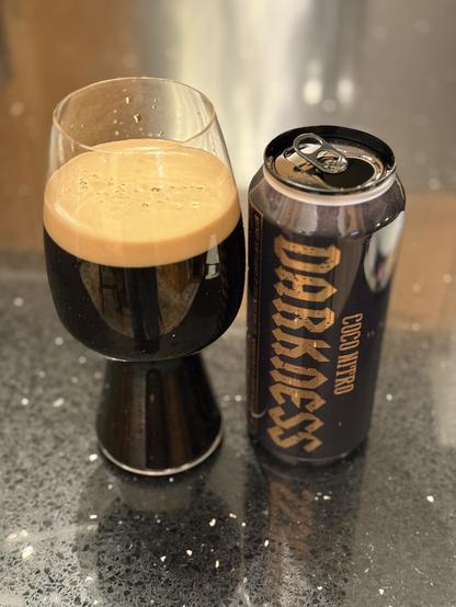 A stout glass of dark beer with a tan head. The black pint can has bold gold lettering saying “coco nitro Darkness”
