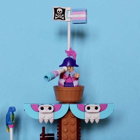 A Lego pirate minifig keeping an eye out from the crow’s nest. On top of the mast wave a pirate flag and a trans flag.
