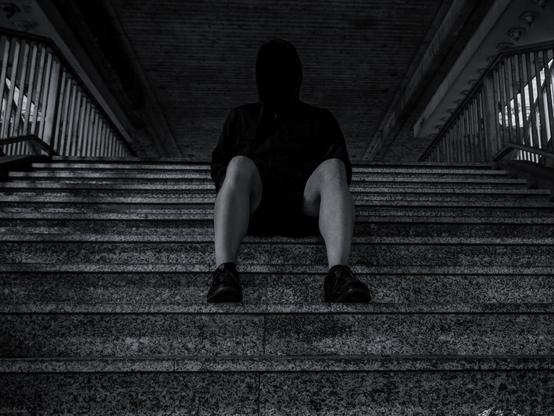ein Typ sitzt im Schatten einer Treppe in einer Unterführung